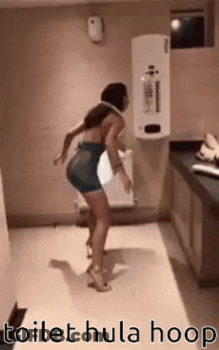 A Woman Is Dancing In A Bathroom With A Toilet Hula Hoop Around Her Waist . GIF