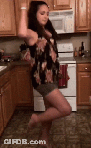 A Woman Is Dancing In A Kitchen In Front Of A Stove . GIF