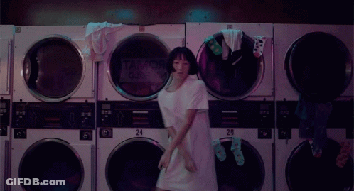 A Woman Is Dancing In A Laundromat With A Sign That Says Tank Queen On It GIF