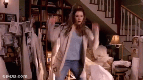 A Woman Is Dancing In A Living Room In Front Of Stairs . GIF