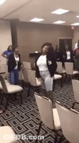A Woman Is Dancing In A Room Full Of Chairs GIF