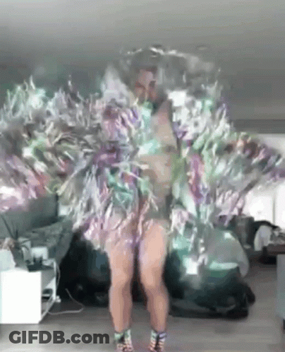 A Woman Is Dancing In A Room Wearing A Feathered Dress . GIF