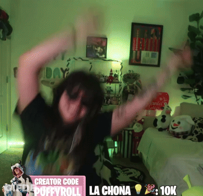 A Woman Is Dancing In A Room With A Sign That Says Creator Code Puffyroll La Chona 10K GIF