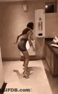 A Woman Is Dancing In A Room With A White Wall And A Heater . GIF