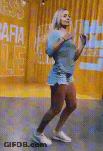A Woman Is Dancing In A Room With A Yellow Curtain And A Sign That Says ' Ara ' On It . GIF