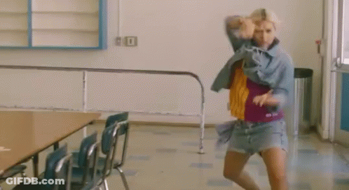 A Woman Is Dancing In A Room With Chairs And A Table . GIF