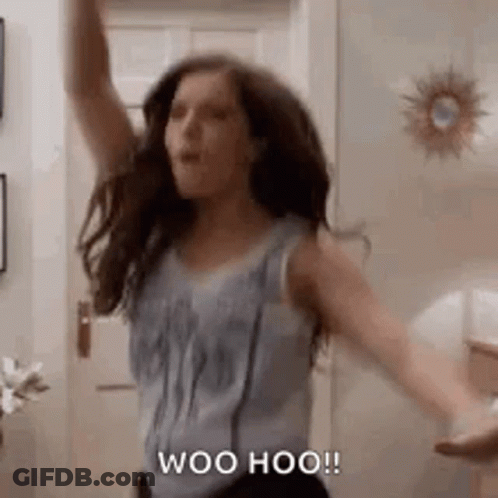 A Woman Is Dancing In A Room With Her Arms In The Air And Saying Woo Hoo . GIF