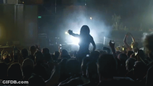 A Woman Is Dancing In Front Of A Crowd At A Concert With A Green Exit Sign In The Background GIF