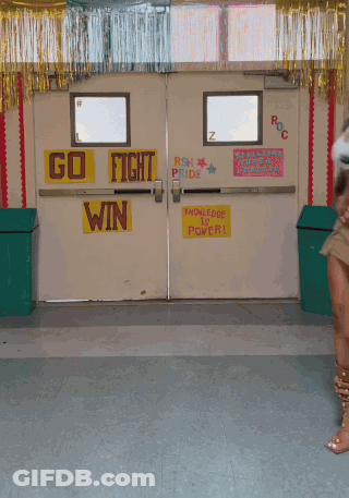 A Woman Is Dancing In Front Of A Door That Says Go Fight Win On It GIF