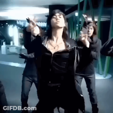 A Woman Is Dancing In Front Of A Group Of People In A Dark Room . GIF