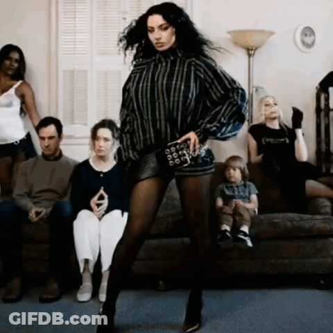 A Woman Is Dancing In Front Of A Group Of People Who Are Sitting On A Couch GIF