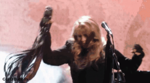 A Woman Is Dancing In Front Of A Microphone While Her Hair Blows In The Wind . GIF