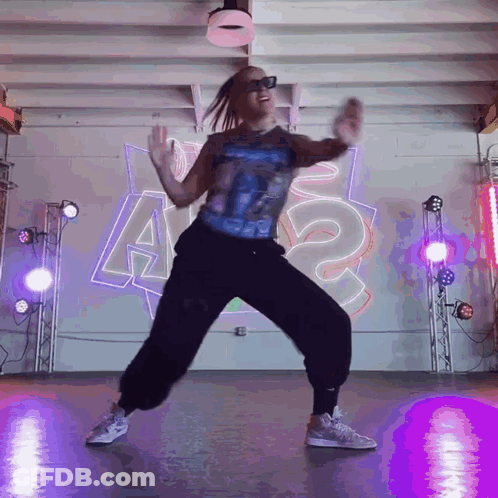 A Woman Is Dancing In Front Of A Wall That Has The Letter A On It GIF