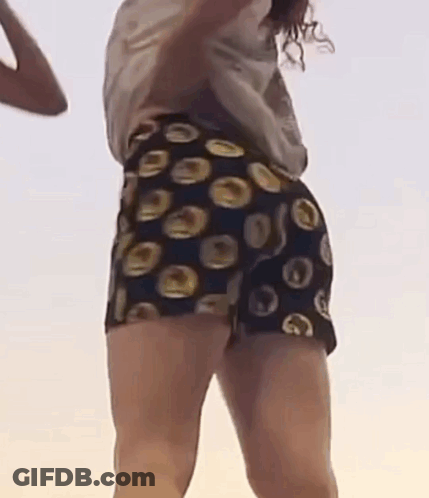 A Woman Is Dancing On A Beach Wearing Shorts With Circles On Them . GIF