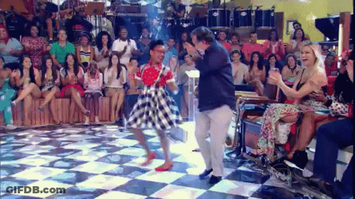 A Woman Is Dancing On A Checkered Floor In Front Of A Crowd Of People . GIF