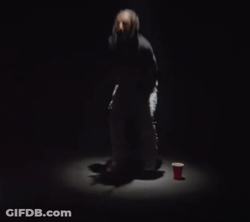 A Woman Is Dancing On A Stage In A Dark Room With A Microphone In Her Hand . GIF