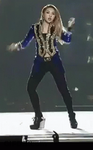 A Woman Is Dancing On A Stage Wearing A Blue Jacket And Black Pants GIF