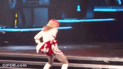 A Woman Is Dancing On A Stage Wearing A White Jacket And Boots . GIF