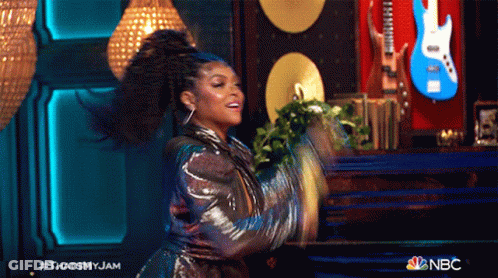 A Woman Is Dancing On A Stage With A Guitar In The Background GIF