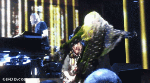 A Woman Is Dancing On A Stage With A Man Playing A Piano Behind Her GIF