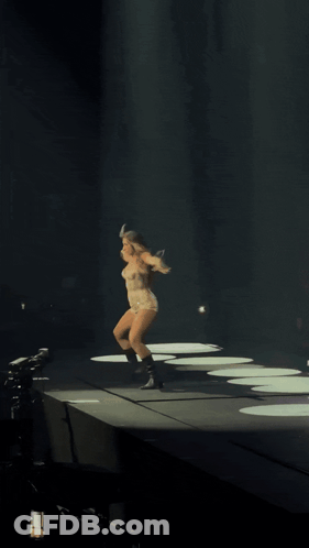 A Woman Is Dancing On A Stage With Her Arms Outstretched In The Dark GIF