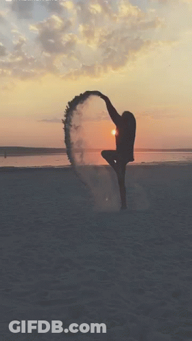 A Woman Is Dancing On The Beach At Sunset With Smoke Coming Out Of Her Feet GIF