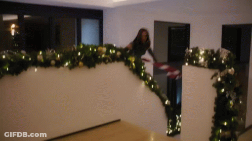A Woman Is Decorating A Staircase With Christmas Decorations . GIF