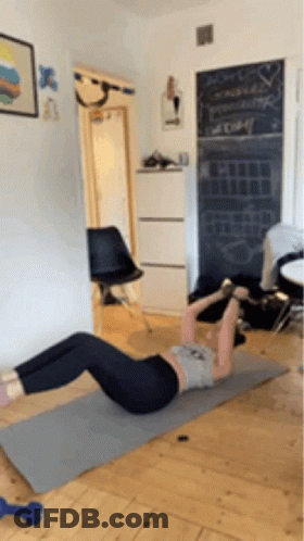 A Woman Is Doing A Crunch On A Yoga Mat In A Room . GIF