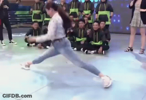 A Woman Is Doing A Trick On A Dance Floor In Front Of A Group Of People Sitting On The Floor . GIF