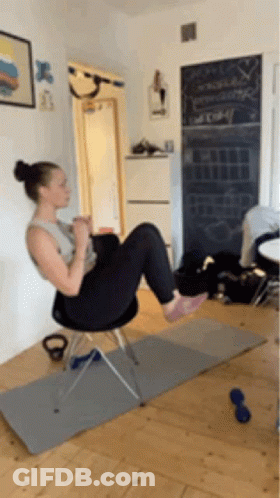 A Woman Is Doing Exercises On A Chair In A Living Room GIF