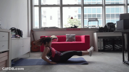 A Woman Is Doing Exercises On A Yoga Mat In Front Of A Red Couch With A Sign That Says " Do Not Enter " GIF
