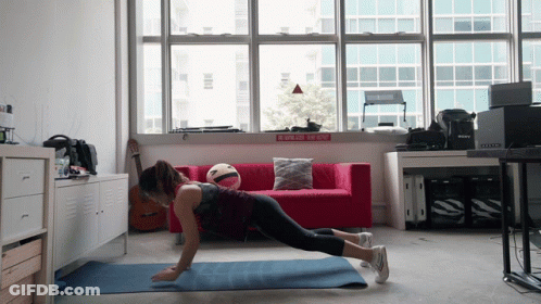 A Woman Is Doing Push Ups On A Yoga Mat In Front Of A Red Couch And A Sign That Says No Smoking GIF