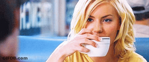 A Woman Is Drinking A Cup Of Coffee While Sitting At A Table In A Restaurant . GIF