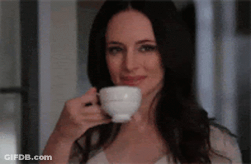 A Woman Is Drinking A Cup Of Coffee While Smiling . GIF
