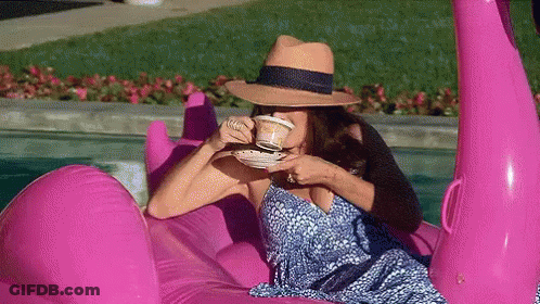 A Woman Is Drinking Coffee While Sitting On A Pink Flamingo Float In A Pool . GIF