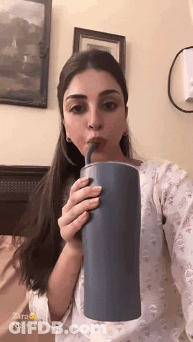 A Woman Is Drinking From A Blue Cup With A Straw And The Name Zara Is On The Bottom GIF