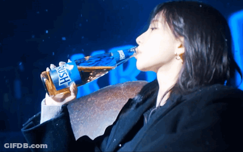 A Woman Is Drinking From A Bottle That Says Rush On It GIF
