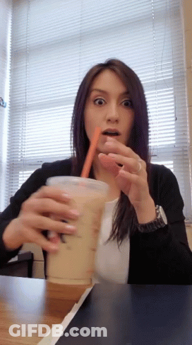 A Woman Is Drinking From A Cup That Says ' Iced Coffee ' On It GIF