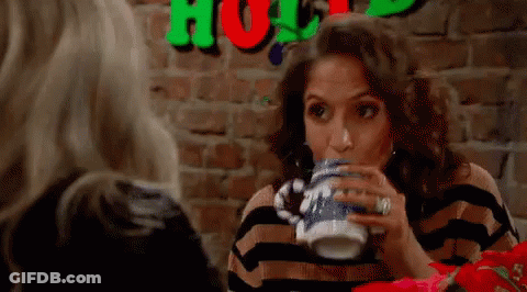 A Woman Is Drinking From A Mug While Sitting At A Table . GIF