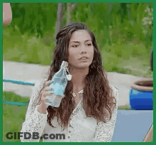 A Woman Is Drinking Water From A Bottle While Sitting On A Bench . GIF