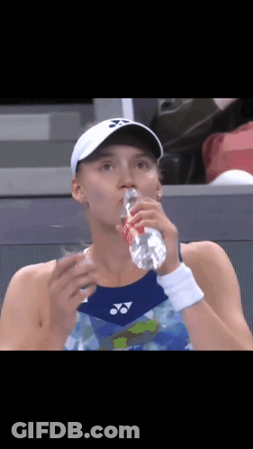 A Woman Is Drinking Water From A Bottle While Wearing A White Hat . GIF
