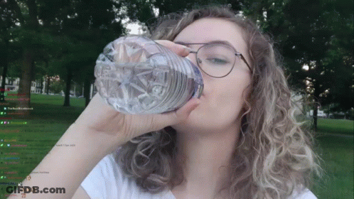 A Woman Is Drinking Water From A Plastic Bottle In Front Of Trees GIF