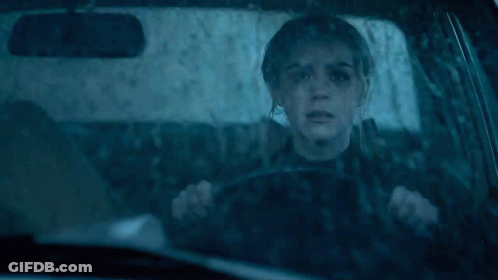 A Woman Is Driving A Car In The Rain With A Reflection Of Her Face In The Windshield GIF