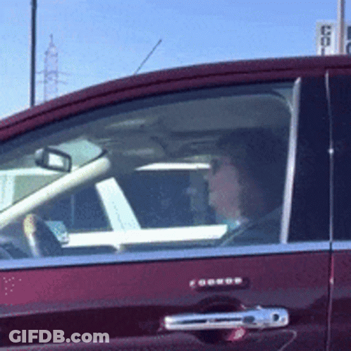 A Woman Is Driving A Red Car With A Sign In The Background That Says ' Coca Cola ' GIF