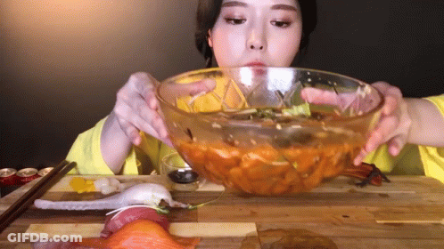 A Woman Is Eating A Bowl Of Food With Chopsticks GIF