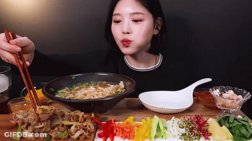 A Woman Is Eating A Bowl Of Noodles With Chopsticks GIF