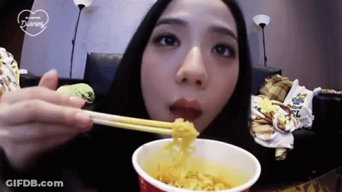 A Woman Is Eating A Cup Of Noodles With Chopsticks GIF