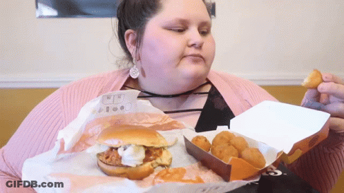 A Woman Is Eating A Hamburger And Chicken Nuggets From A Box GIF
