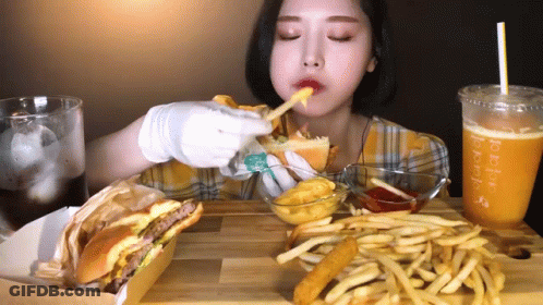 A Woman Is Eating A Hamburger And French Fries At A Table With A Drink That Says ' Peach ' On It GIF