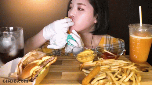 A Woman Is Eating A Hamburger And French Fries With A Drink That Says Purple GIF